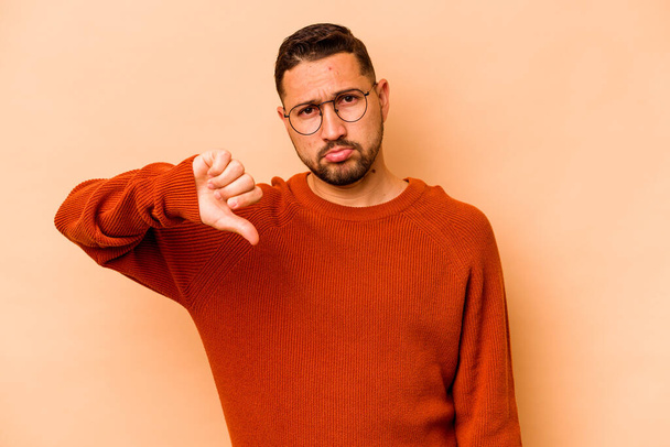 Young hispanic man isolated on beige background showing a dislike gesture, thumbs down. Disagreement concept. - Photo, Image