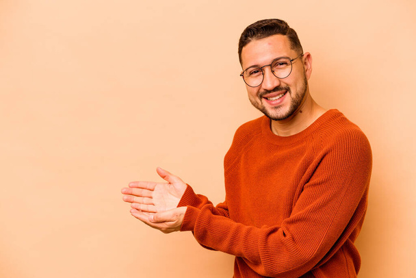 Young hispanic man isolated on beige background holding a copy space on a palm. - Foto, Imagem
