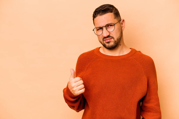 Young hispanic man isolated on beige background shocked pointing with index fingers to a copy space. - Foto, Imagen