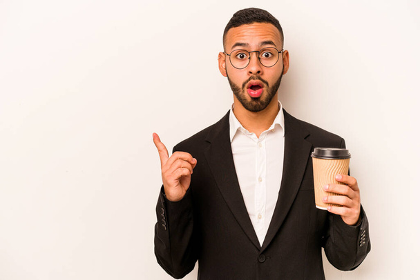 Junger hispanischer Geschäftsmann hält Kaffee zum Mitnehmen isoliert auf weißem Hintergrund, der zur Seite zeigt - Foto, Bild