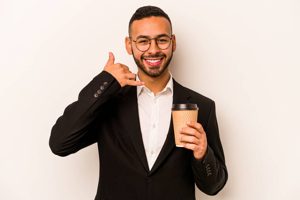 Joven empresario hispano sosteniendo café para llevar aislado sobre fondo blanco mostrando un gesto de llamada telefónica móvil con los dedos. - Foto, Imagen
