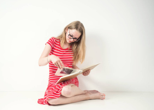 Блондинка в красно-полосатом платье с очками и книгой на белом фоне. - Фото, изображение