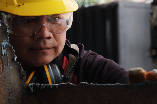 Mężczyzna pracownik noszący okulary i rękawice budowlane sprawdza pracę po szlifowaniu metalu szlifierką kątową w warsztacie domowym. - Zdjęcie, obraz