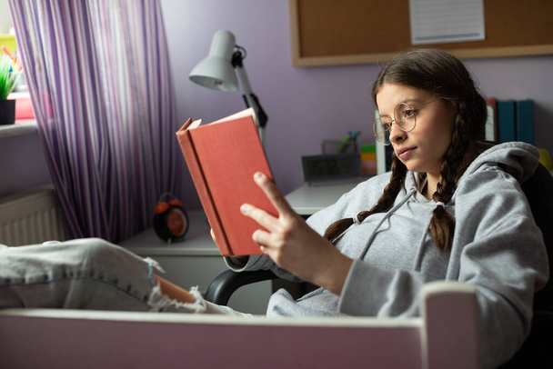 A teenage girl with glasses reads her next school reading with interest. - Zdjęcie, obraz