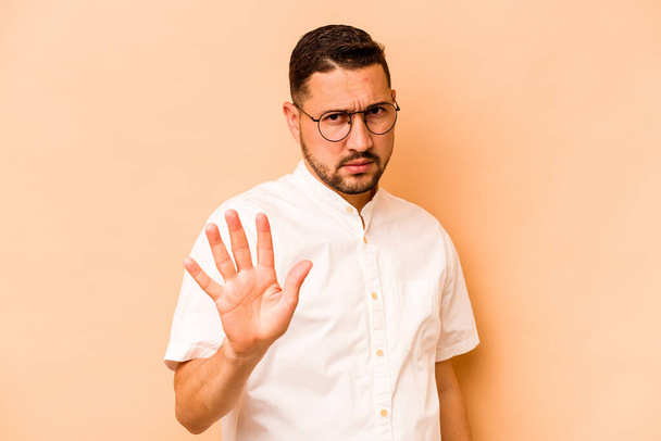 Joven hombre hispano aislado sobre fondo beige rechazando a alguien mostrando un gesto de disgusto. - Foto, Imagen