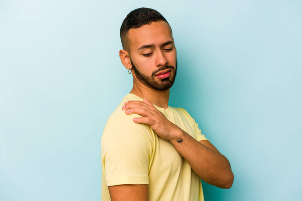 Mavi arka planda izole edilmiş genç İspanyol bir adam omuz ağrısı çekiyor.. - Fotoğraf, Görsel