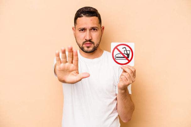 Hispanic caucasian man holding no eating sign isolated on beige background - Photo, Image