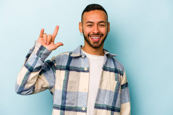 Young hispanic man isolated on blue background showing a horns gesture as a revolution concept. - 写真・画像