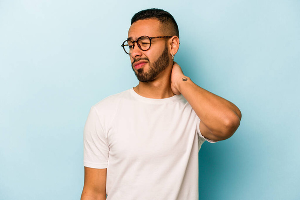 Young hispanic man isolated on blue background having a neck pain due to stress, massaging and touching it with hand. - Photo, Image