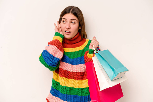 Giovane donna caucasica andare a fare shopping isolato su sfondo bianco cercando di ascoltare un pettegolezzo. - Foto, immagini