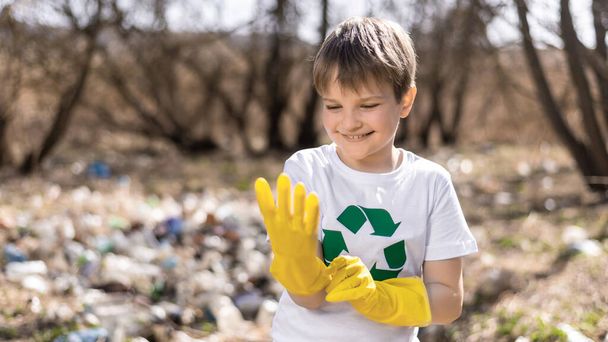 Ragazzo indossare guanti di gomma per la raccolta dei rifiuti di plastica in una radura inquinata, segno di riciclaggio sulla T-shirt - Foto, immagini