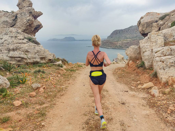 Блондинка в спортивной одежде бегает по горной тропе. Летние каникулы в Греции - Фото, изображение