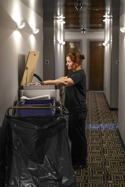 Uklízecí vozík s čisticím vybavením a hospodyní v hotelu na chodbě. Úklidový vozík s čisticím vybavením v hotelu na chodbě. Pohled na hotelovou chodbu - Fotografie, Obrázek