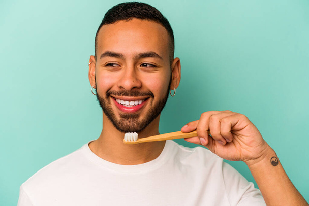 青の背景に孤立した歯ブラシを身に着けている若いヒスパニック系の男 - 写真・画像