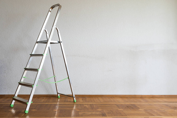 Escalera de cromo plegable contra pared en blanco en interiores
 - Foto, Imagen