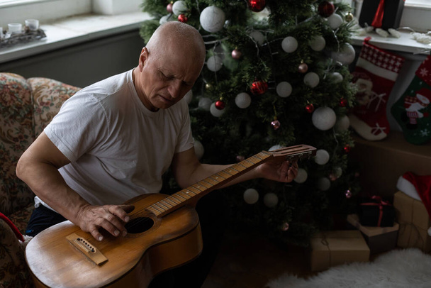 Happy people rodinný koncept - Starý senior muž těší kytaru na pohovce v domě na Vánoce - Fotografie, Obrázek
