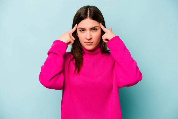 Young caucasian woman isolated on blue background focused on a task, keeping forefingers pointing head. - Photo, Image