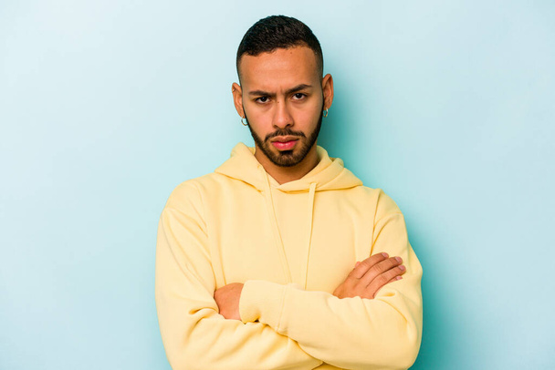 Young hispanic man isolated on blue background frowning face in displeasure, keeps arms folded. - Foto, imagen