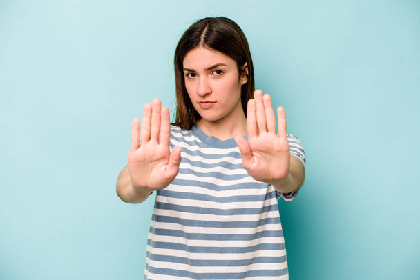 Nuori valkoihoinen nainen sinisellä taustalla seisoo ojennetulla kädellä osoittaa stop-merkki, estää sinua. - Valokuva, kuva