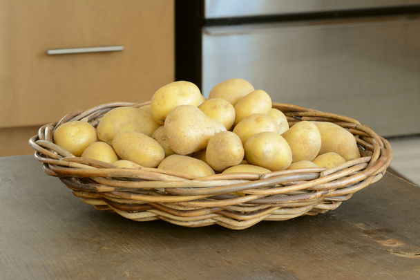 Φρέσκιες πατάτες κίτρινο στο υφαμένο καλάθι στον πίνακα κουζίνες - Φωτογραφία, εικόνα