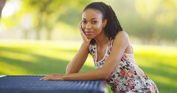 Μαύρη γυναίκα που κάθεται σε ένα πάρκο πάγκος χαμογελώντας - Φωτογραφία, εικόνα