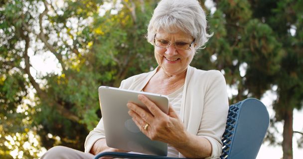 Старшая женщина счастливо серфинг в Интернете на планшете в парке
 - Фото, изображение