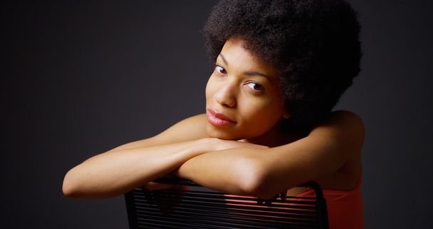Femme noire souriante assise avec les bras sur le dossier de la chaise
 - Photo, image