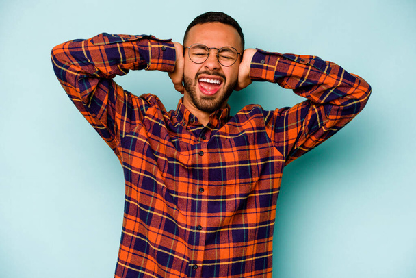 Young hispanic man isolated on blue background covering ears with hands trying not to hear too loud sound. - Foto, imagen