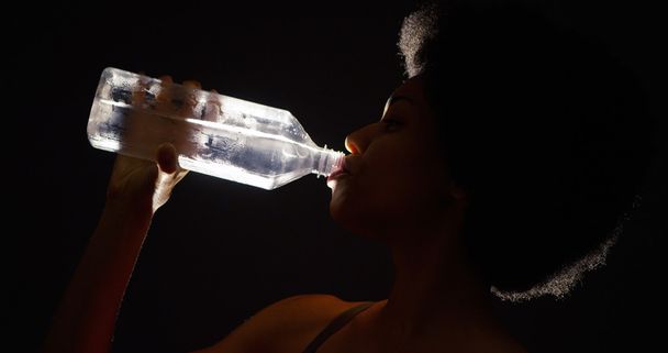 Estudio retroiluminado de mujer negra bebiendo agua de la botella
 - Foto, imagen