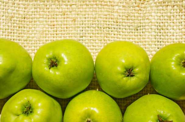 Зеленые яблоки крупным планом на фоне ткани в лучах солнечного света - Фото, изображение