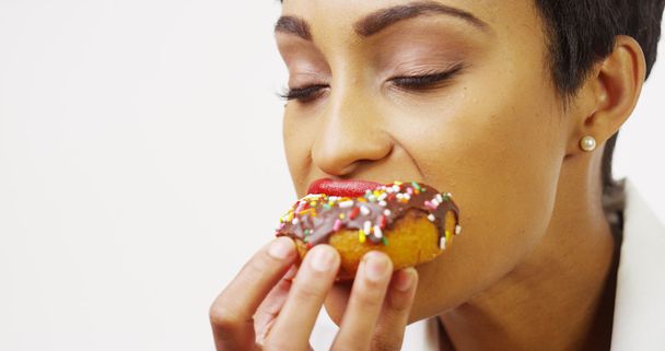 Mulher afro-americana se entregando em delicioso donut de chocolate com polvilhas
 - Foto, Imagem