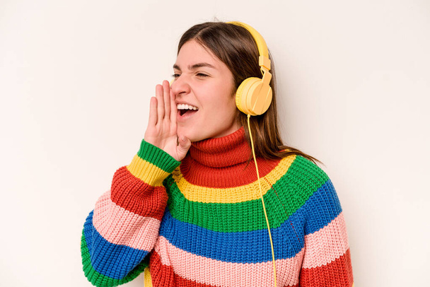 Nuori valkoihoinen nainen kuuntelee musiikkia eristetty valkoisella taustalla huutaa ja pitää kämmen lähellä avattu suu. - Valokuva, kuva