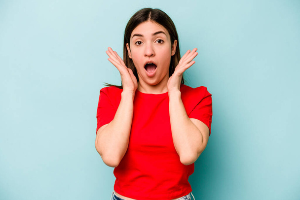 Young caucasian woman isolated on blue background surprised and shocked. - 写真・画像