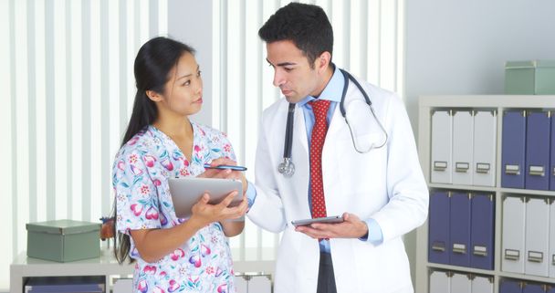 Médico mexicano hablando con enfermera asiática con tabletas
 - Foto, Imagen