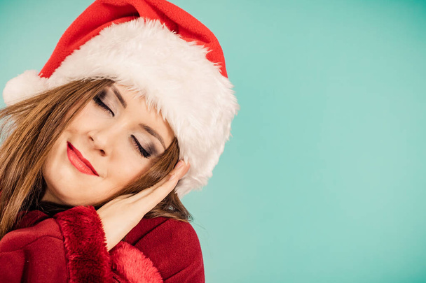 Tired woman wearing santa hat gesturing sleep gesutre with her hands. Adult female being sleepy, ready to take a nap. Christmas time. - Foto, afbeelding