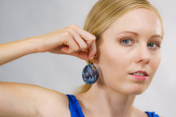 Girl holding blue plum to her ear. Healthy seasonal fruits. Raw food diet. Making jewelry from fruit. - Photo, Image