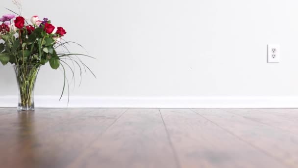 Powoli przesuwane przed układem kwiatów róż umieszczone na drewnianej podłodze przed białą ścianą z gniazdkiem zasilania i płyty bazowej - Materiał filmowy, wideo