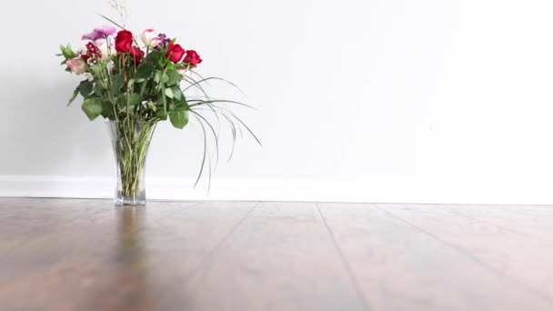 Deslizando da direita para a esquerda na frente de arranjo floral colocado no chão de madeira de uma sala vazia com parede branca - Filmagem, Vídeo