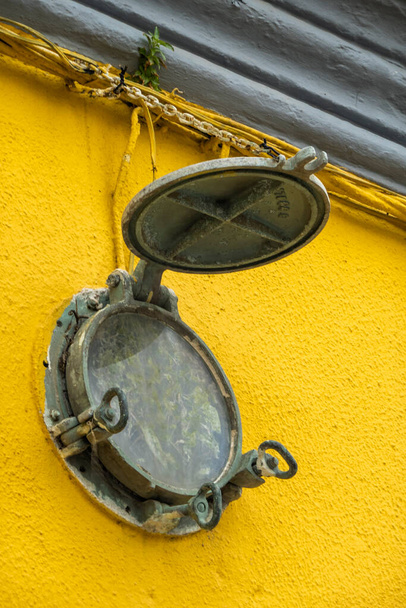 Zardzewiałe stare okrągłe okno marynarki na żółtej ścianie. - Zdjęcie, obraz