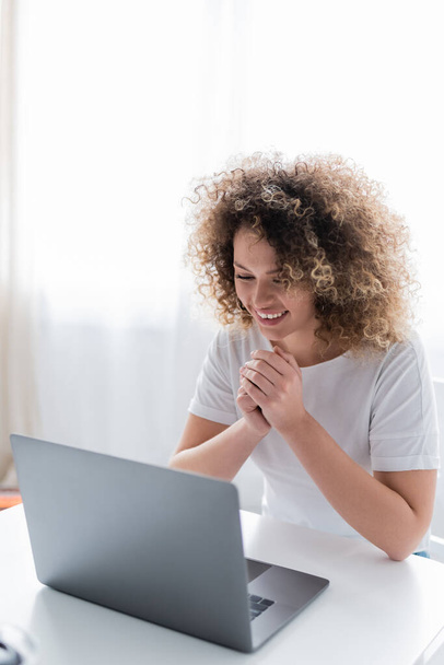 joven mujer asombrada mirando a la computadora portátil mientras tiene videollamada en casa - Foto, imagen