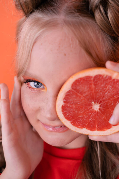 Csinos tinilány narancssárga ruhában, narancssárga alapon elszigetelt grapefruittal. trópusi citrusfélék Grapefruit szeletek. narancssárga stílusos smink. tinédzser portré. - Fotó, kép