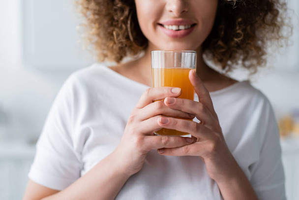 cropped view of curly smiling woman holding glass of fresh orange juice - Foto, Bild