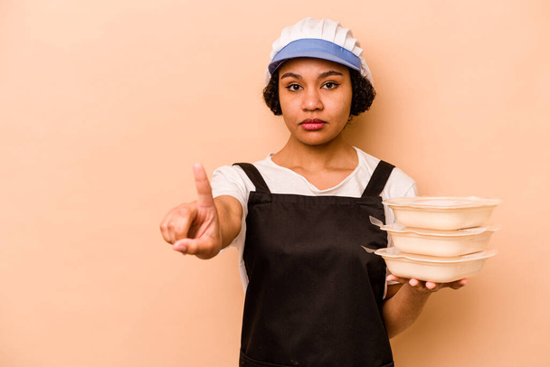 Mladý kuchař dobrovolník Afroameričanka izolované na béžové pozadí ukazující číslo jedna s prstem. - Fotografie, Obrázek