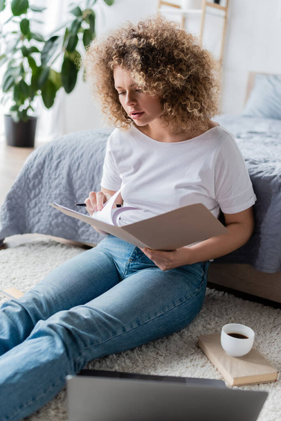 young woman with documents working on floor near laptop and coffee cup - Фото, зображення