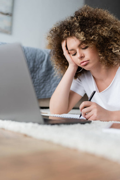 töprengő nő írásban notebook közelében elmosódott laptop padlón a hálószobában - Fotó, kép