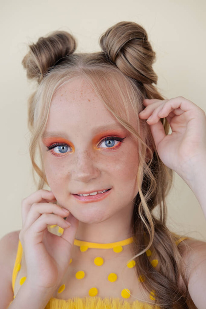 charming blonde tween girl with orange makeup on yellow background. teenager portrait. - Photo, Image