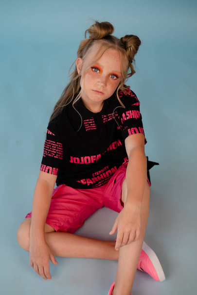 stijlvol tienermeisje. tussen school meisje draagt roze mode kleding op een blauwe achtergrond. lang haar en sproeten. - Foto, afbeelding