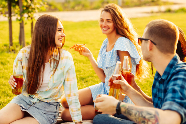 group of friends are enjoying pizza in the park. Men and women sit on the grass around a pizza box. The concept of a picnic in the park, friends together in nature - Фото, зображення