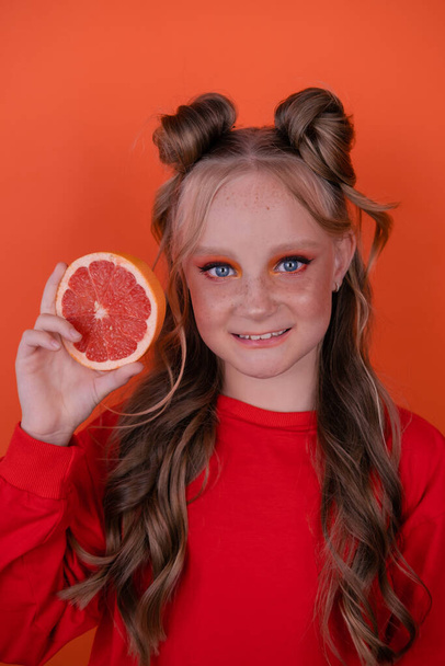 graziosa ragazza in arancione con un pompelmo isolato su sfondo arancione. agrumi tropicali Fette di pompelmo. arancio trucco elegante. ritratto adolescente. - Foto, immagini