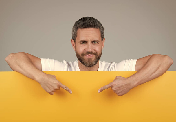 здоровый зрелый бородатый мужчина за желтой бумагой указывать пальцами на копировальный пейзаж, предложение - Фото, изображение